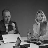 A person and person sitting at a table with laptops and a bottle of waterDescription automatically generated