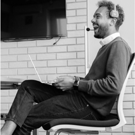 A person sitting in a chair with a computer and headsetDescription automatically generated