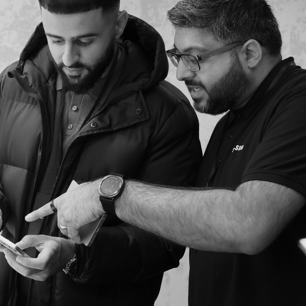 A couple of men looking at a cellphoneDescription automatically generated