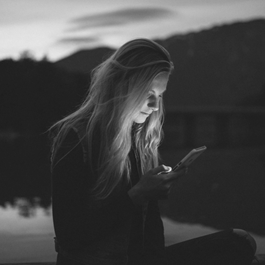 A person sitting on a dock looking at her phoneDescription automatically generated